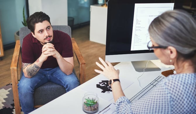 A business owner listens as an advisor gestures toward a report on her monitor, taking in outside perspective during a one-on-one review.
