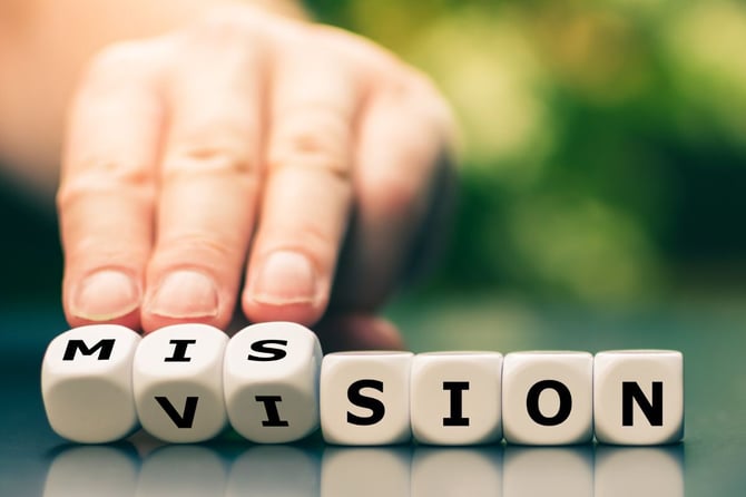 Hand tipping white letter dice to change the word "mission" into "vision," symbolizing a business owner shifting focus toward a clear company vision