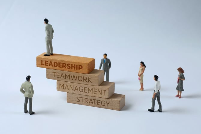 figures stand among wooden blocks while on sits atop a block labeled "leadership"