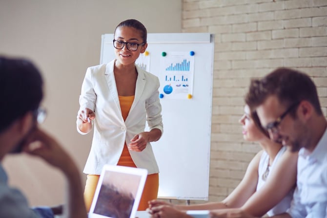 small business owner leading a team meeting in front of a whiteboard with charts