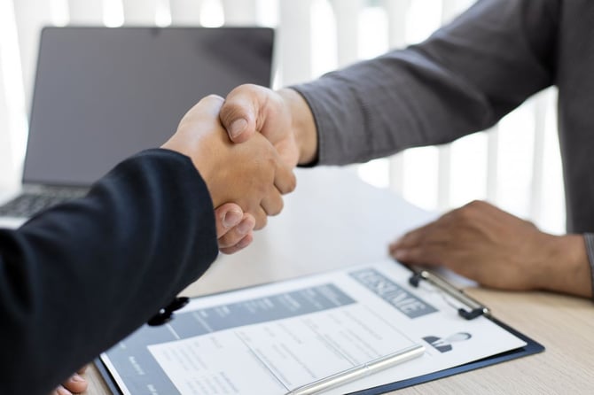 A hiring manager and job candidate shake hands across a desk after an interview
